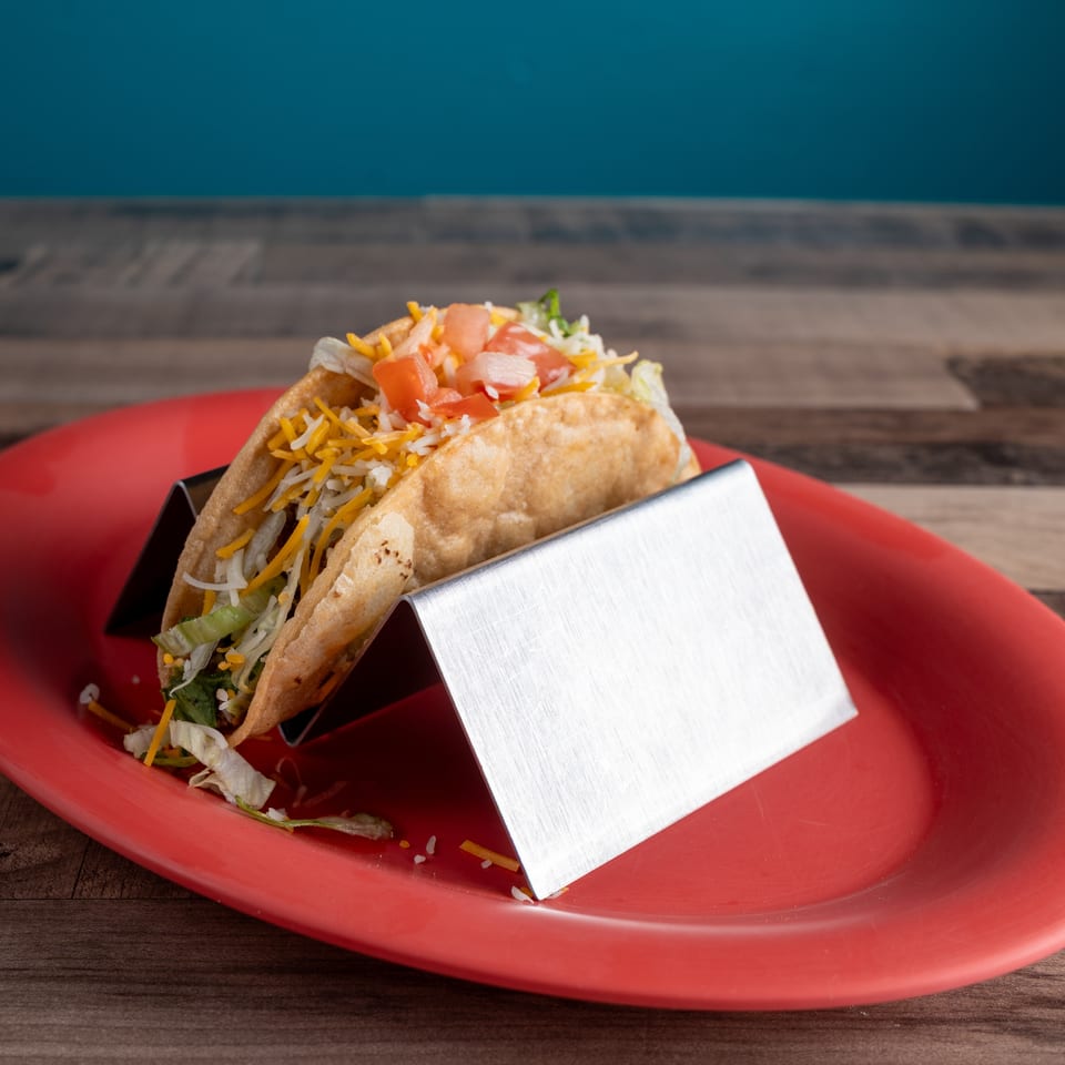 A crispy taco filled with lettuce, cheese, and diced tomatoes, served on a red plate.