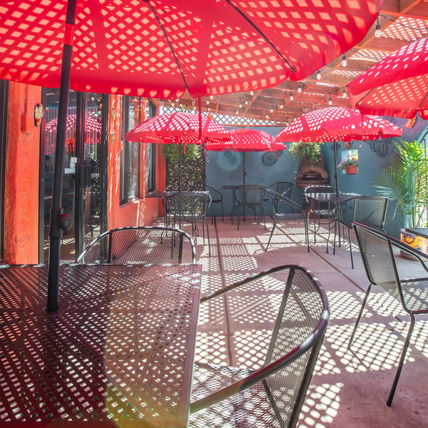 Outdoor patio with red umbrellas casting patterned shadows over black mesh tables and chairs.