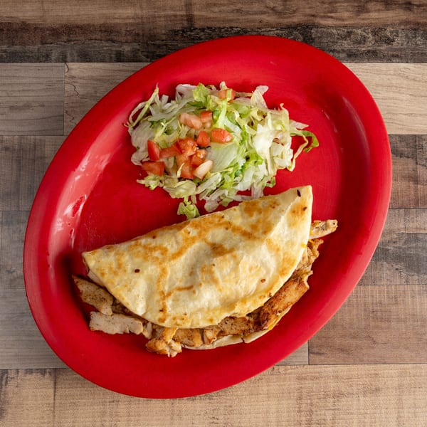 Chicken quesadilla with a side of shredded lettuce and diced tomatoes on a red plate.