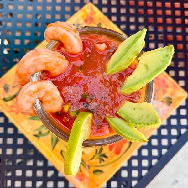 Shrimp cocktail with avocado slices and lime, served on a colorful plate on a dark patio table.
