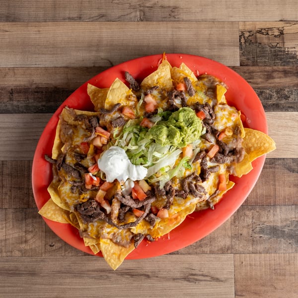 A large platter of steak nachos with cheese, refried beans, guacamole, sour cream, and pico de gallo.