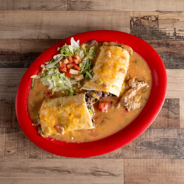 Two burritos covered in cheese sauce, with lettuce and diced tomatoes, on a red plate.