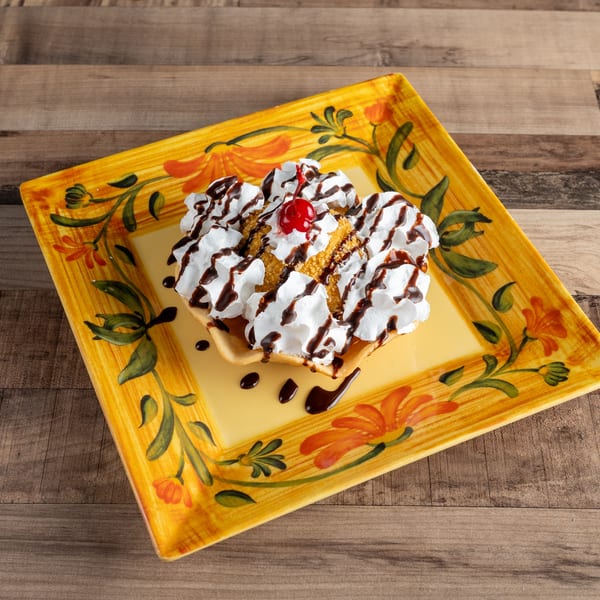 Fried ice cream dessert with whipped cream, chocolate syrup, and a cherry on a decorative yellow plate.