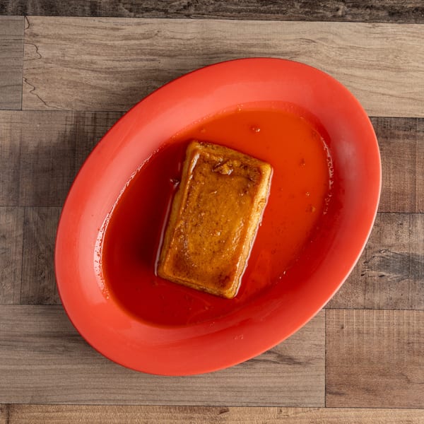 Rectangular flan dessert with caramel sauce on a red oval plate, on a wooden table.