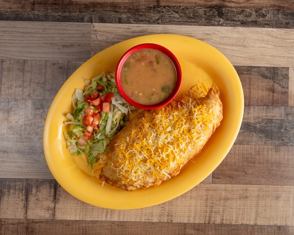 Golden fried chimichanga topped with shredded cheese, served with a side of lettuce, tomatoes, and soup.