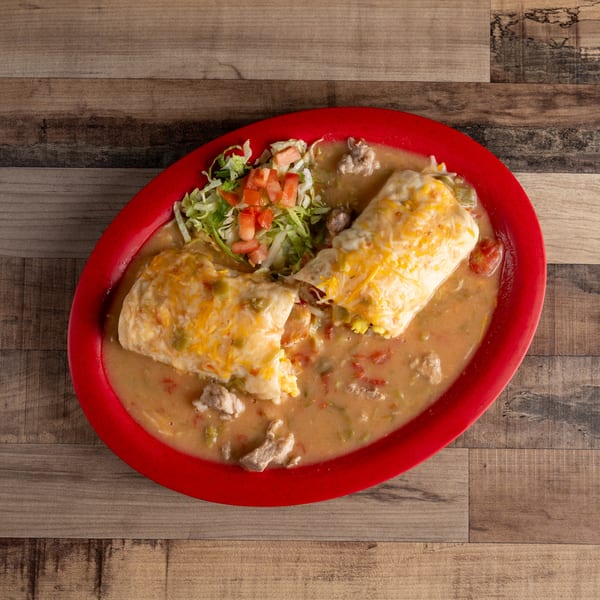 Two cheesy burritos covered in green chili sauce, with a side of shredded lettuce and diced tomatoes.