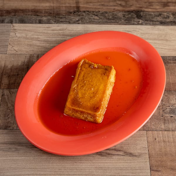 A rectangular flan dessert with caramel sauce on a red oval plate, on a wooden table.