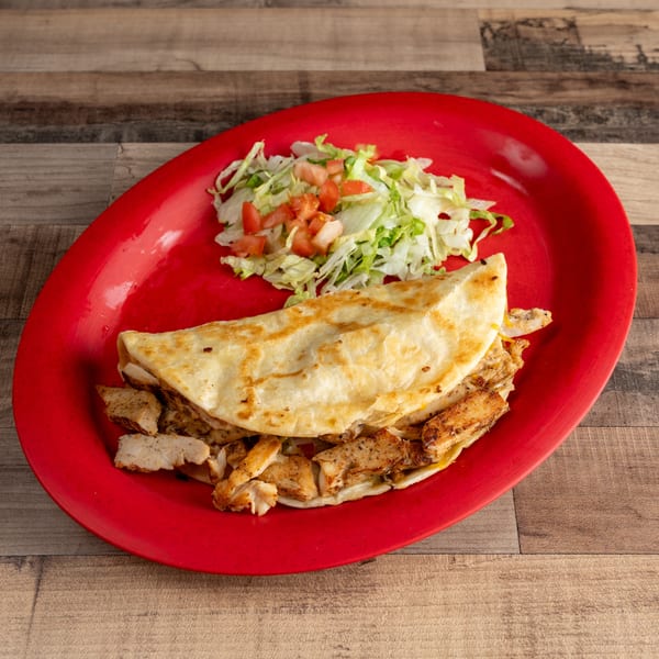 Chicken quesadilla with shredded lettuce and diced tomatoes on a red oval plate.