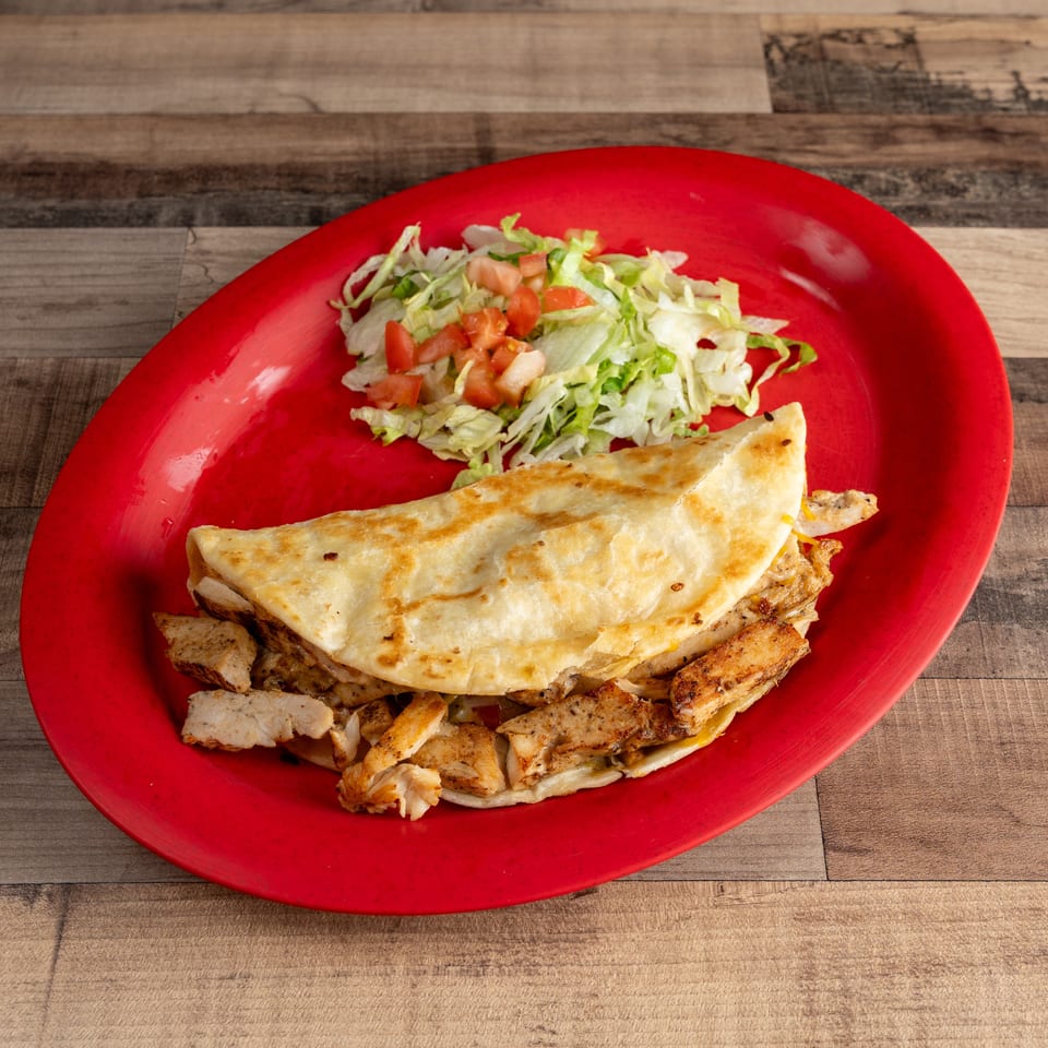 Chicken quesadilla with shredded lettuce and diced tomatoes on a red oval plate.