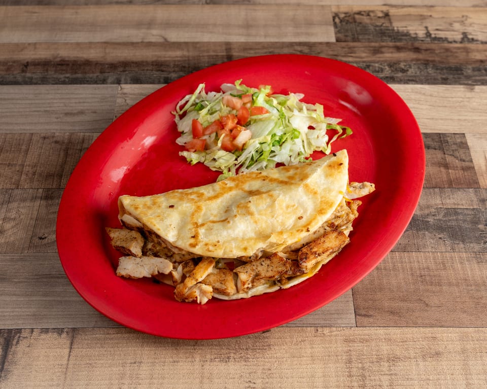 Chicken quesadilla with shredded lettuce and diced tomatoes on a red oval plate.