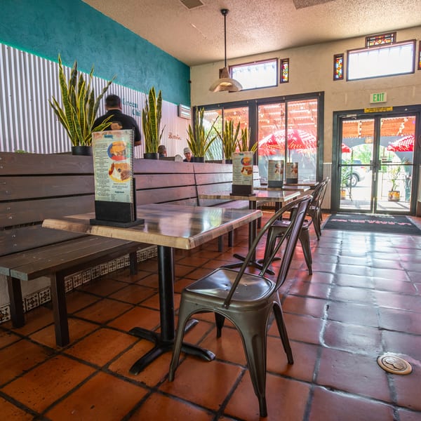Restaurant interior with wooden benches, metal chairs, tiled floors, and menus on tables.