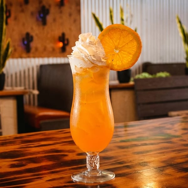 Orange cocktail with whipped cream and an orange slice on a wooden table in a restaurant.