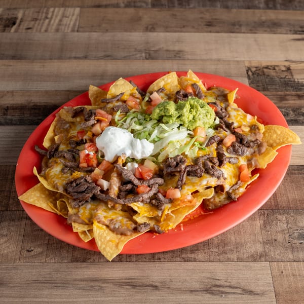 A vibrant red plate piled high with steak nachos, topped with guacamole, sour cream, and fresh vegetables.